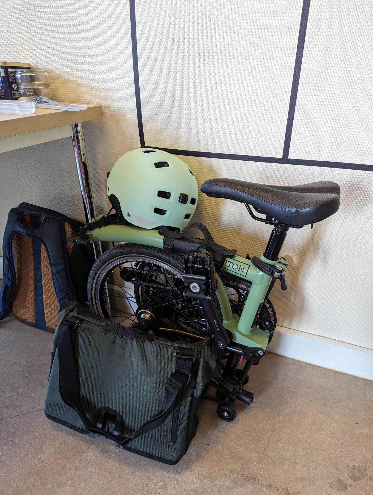 Un vélo Brompton plié, en intérieur, avec un casque et jne sacoche